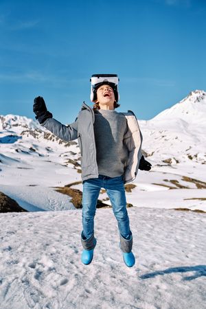Cheerful boy jumping on snowy hill in VR