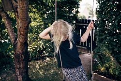Blonde girl with braided hair looking down while standing on outdoor swing