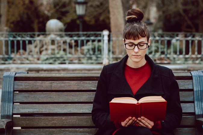 Young woman reading book on bench in park
