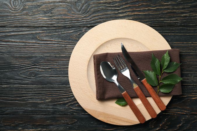 Table setting with wooden plate and cutlery on wooden background