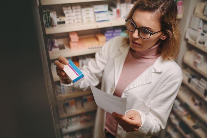 Chemist with a prescription searching right medicine on shelves in pharmacy