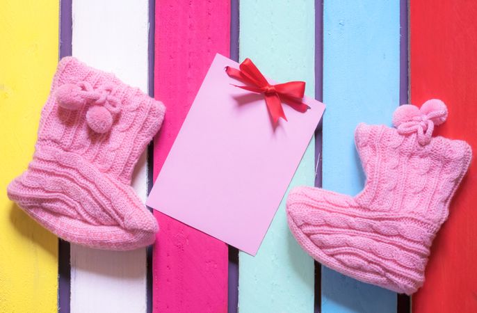 Flat lay of knitted booties and a blank pink paper note