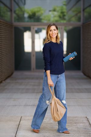 Stylish female standing outside door with thermos and bag