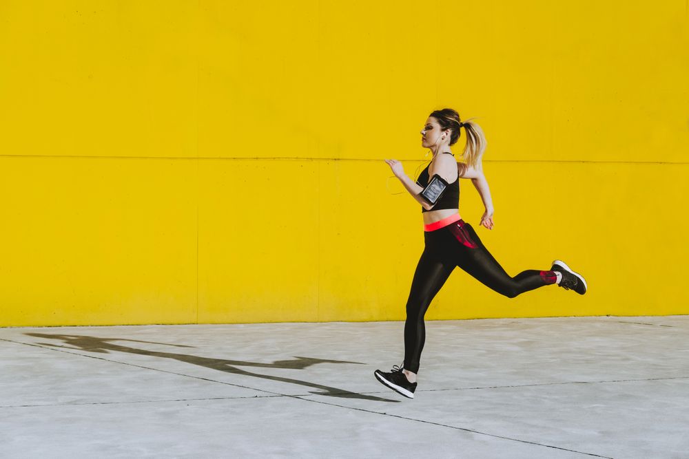 Woman with earphones running near wall