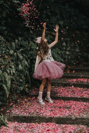 Girl in pink tutu standing on pink petals on ground beside trees