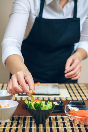 Chef reaching for avocado from bowl as she prepares sushi rolls