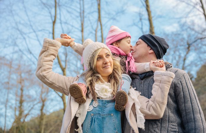 Girl on mother's shoulders as father gives her a kiss