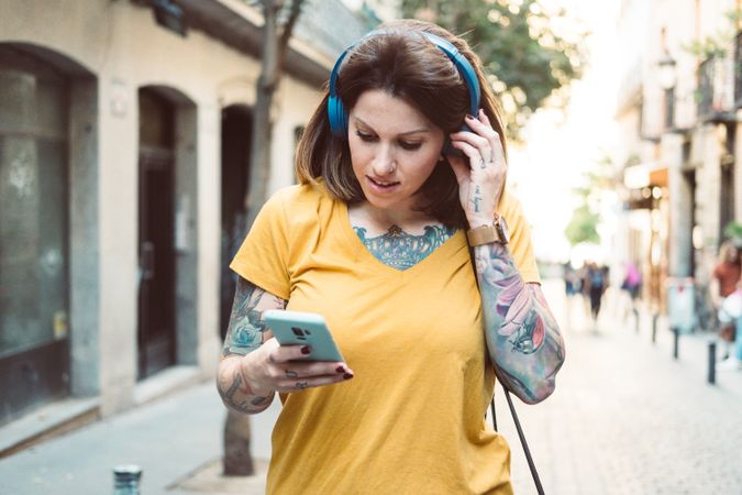 Inspired woman in headphones listening to music on smartphone on street