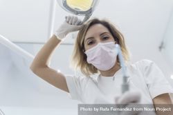 Dentist wearing surgical mask while holding angled mirror and drill, ready to begin 4Npxg0