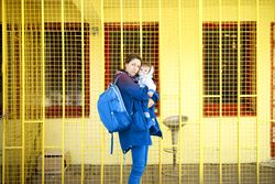Woman in blue standing with her child in front of yellow wall