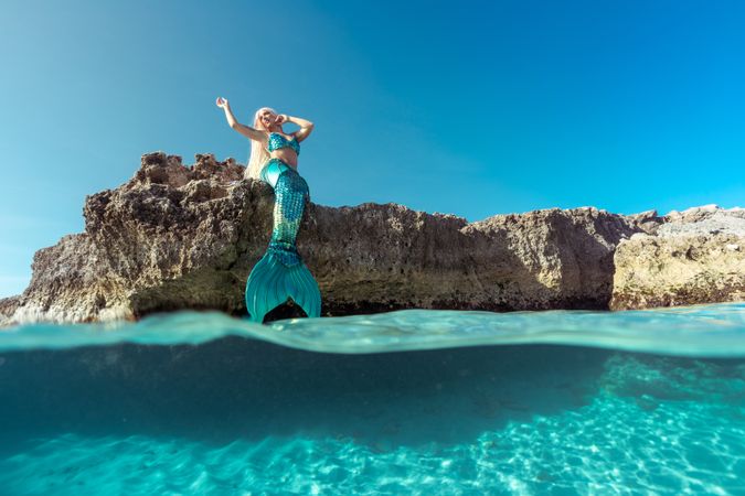 Blond fairytale female mermaid lying on rock