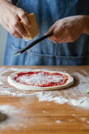 Crop cook grinding cheese on pizza