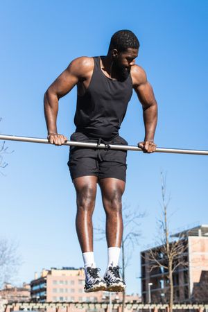 Strong Black sportsman working out on bar in town