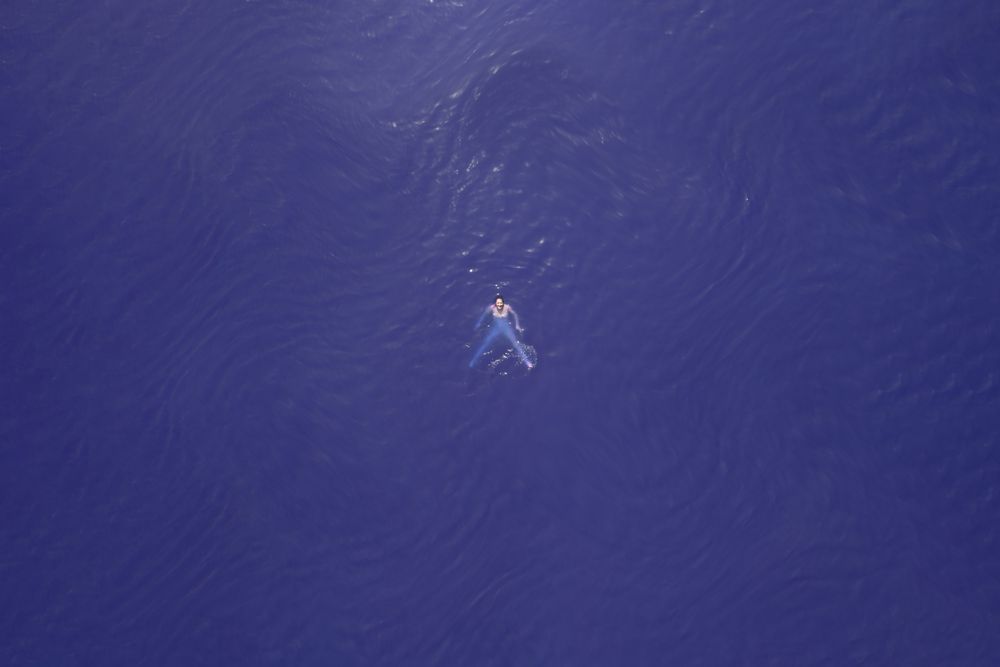 Far away aerial image of woman swimming in purple water