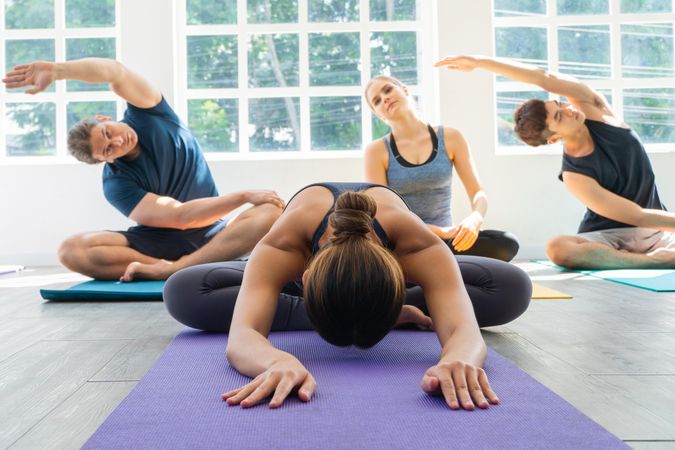 Woman stretching on floor in front of people stretching their arms