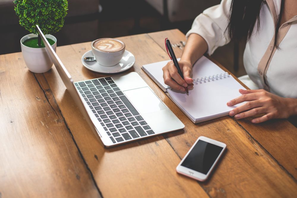 Woman working on wooden table in cafe with cappuccino & phone
