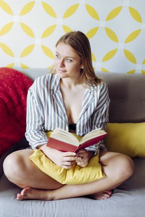Young happy female reading book on sofa