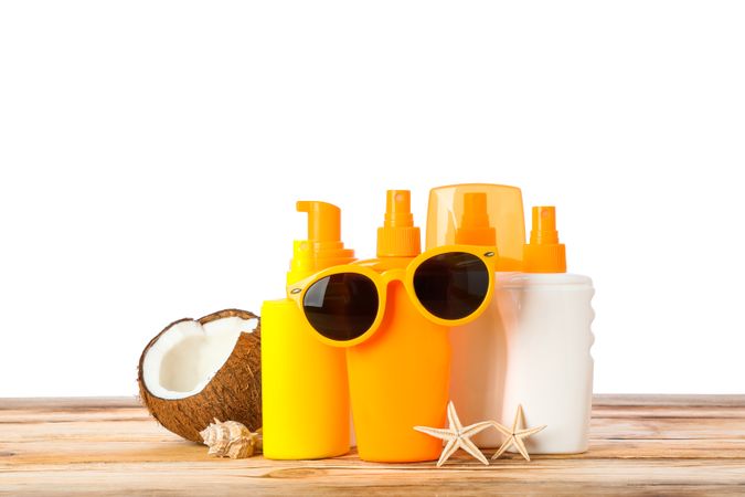Sunscreen sprays with starfishes, coconut and sunglasses on wooden table isolated on plain background. Safe tan