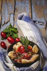 Bowl of delicious ravioli with tomato sauce and rosemary on shabby table