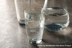 Glasses of water and pitcher on grey marble table 0LGaeb