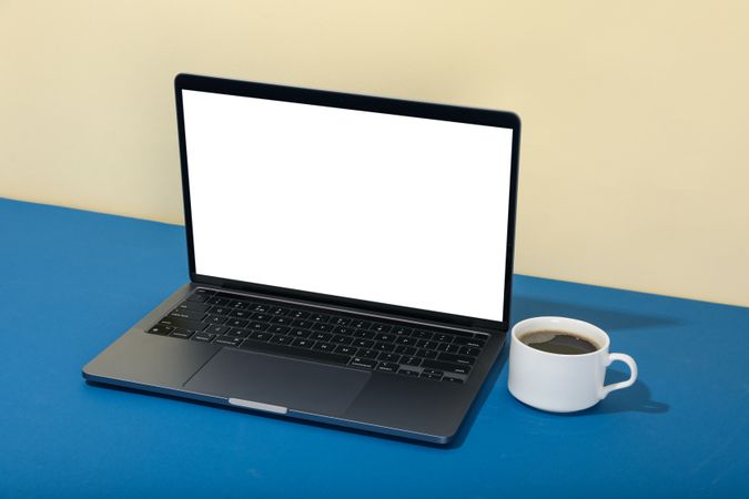 Open laptop with blank mockup screen in cream and blue room with cup