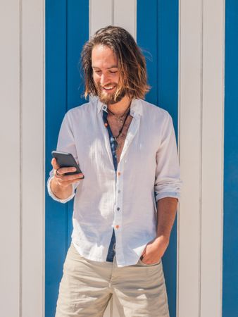 Smiling man browsing smartphone against striped wall
