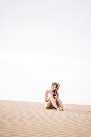 Thoughtful woman using smartphone in desert
