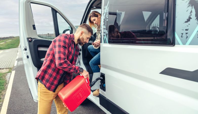 Male in red checkered shirt filling up van with gas can