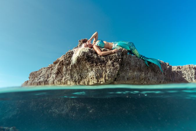 Blond fairytale female mermaid lying on rock