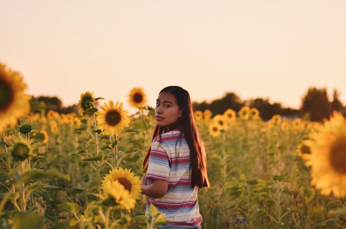 Portrait of woman standing in a sunflower field looking back