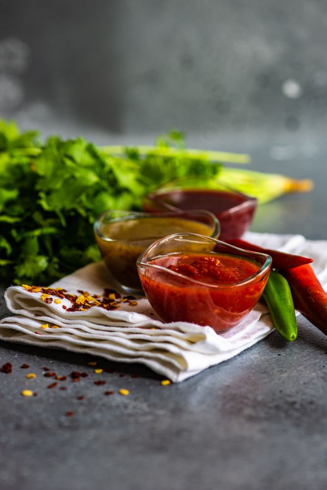 Side view of traditional Georgian sauces tomato satsebeli, yellow and red tkemali with ingredients on stone background with copy space