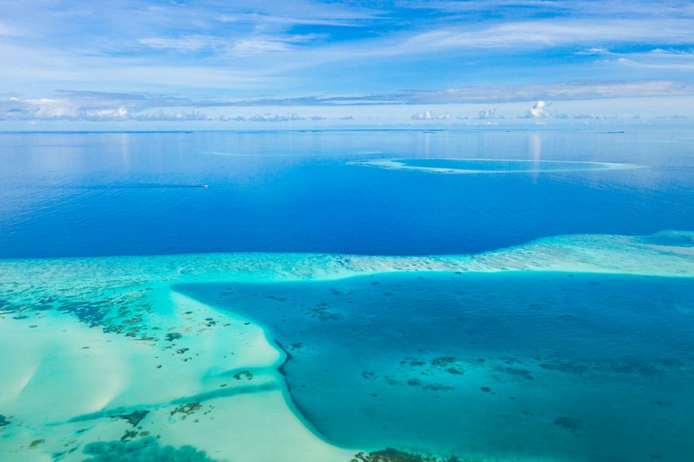 Details of sand and coral in the blue waters of the Maldives under a blue sky with clouds