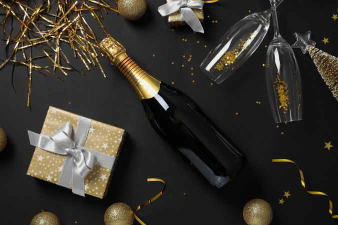 Champagne bottle, glasses and christmas baubles on dark background, top view