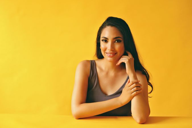 Smiling Hispanic woman resting chin on her hand and sitting in yellow room