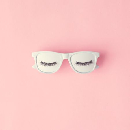 Face of false eyelashes on sunglasses on pink background