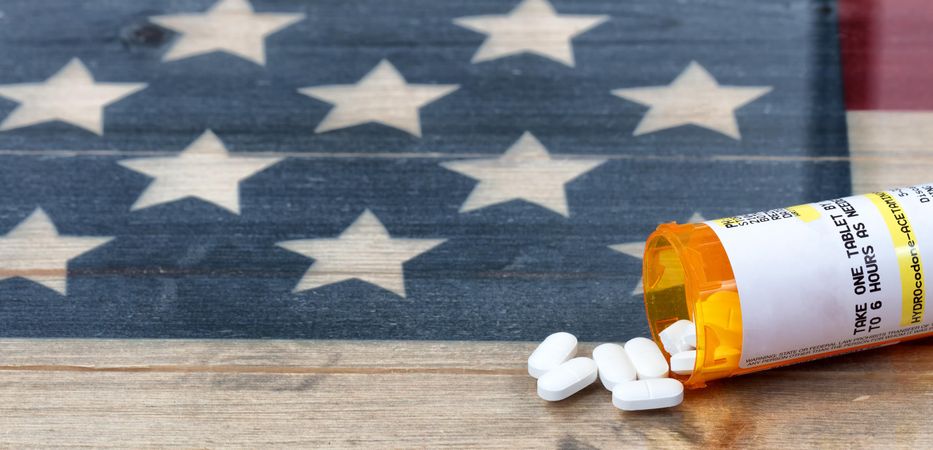 Open prescription bottle of opioid pain killer tablets on USA rustic flag