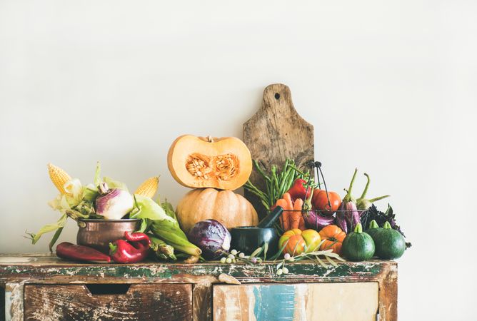 Fresh autumnal vegetables on kitchen counter, with halved squash, cabbage, peppers, corn