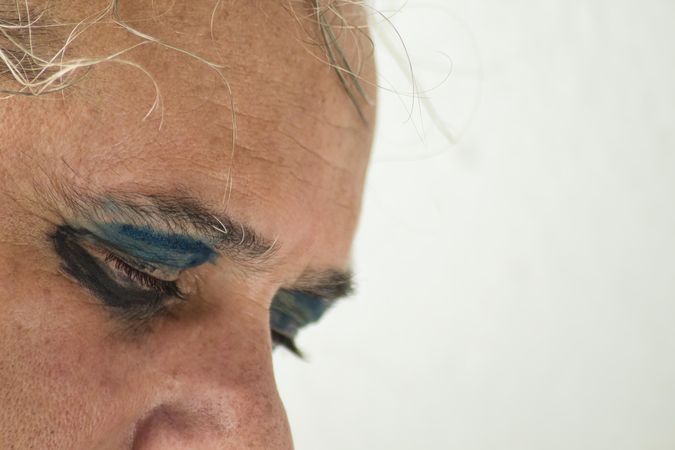 Middle aged man with dark and blue eyeshadow on his closed eyes