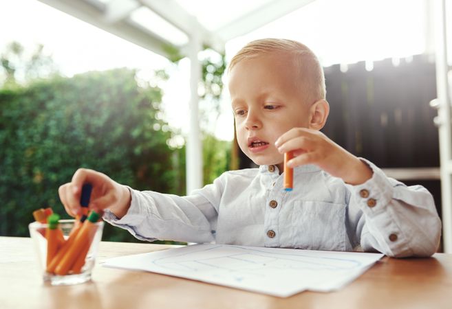 Smiling blond boy drawing outside on deck with crayons