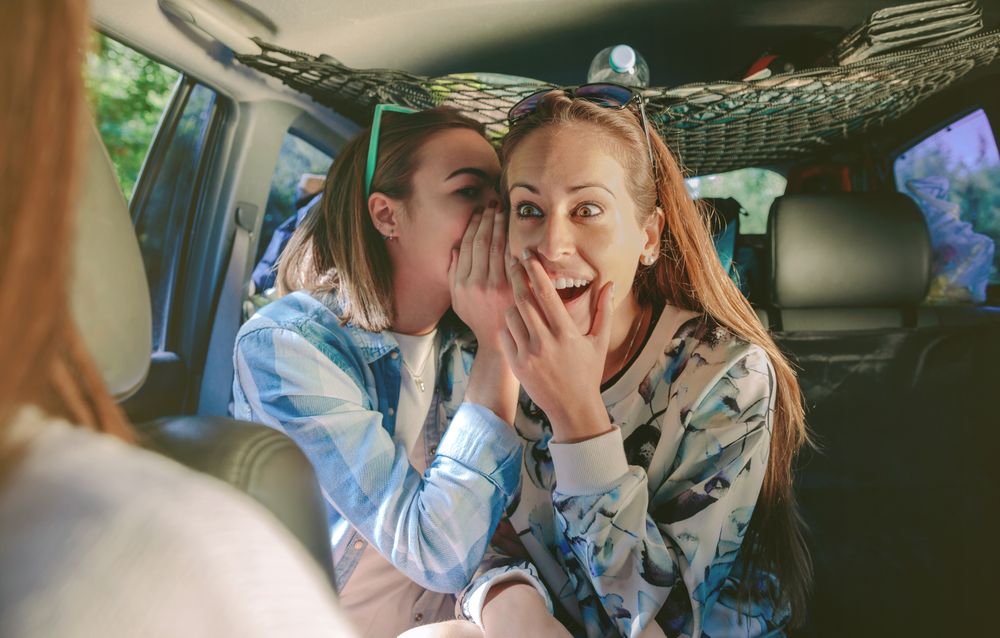 Surprised woman laughing to listening gossip of friend