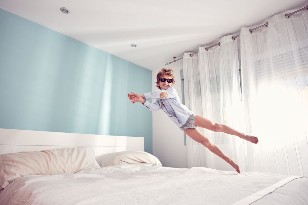Joyful boy jumping on bed in morning