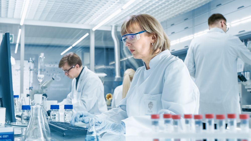 Female Scientist Analyzes Liquid in the Beaker and Types Down Observations on Her Computer.