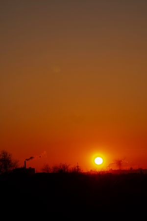 Fiery orange sunset over industrial skyline with silhouetted factory smoke