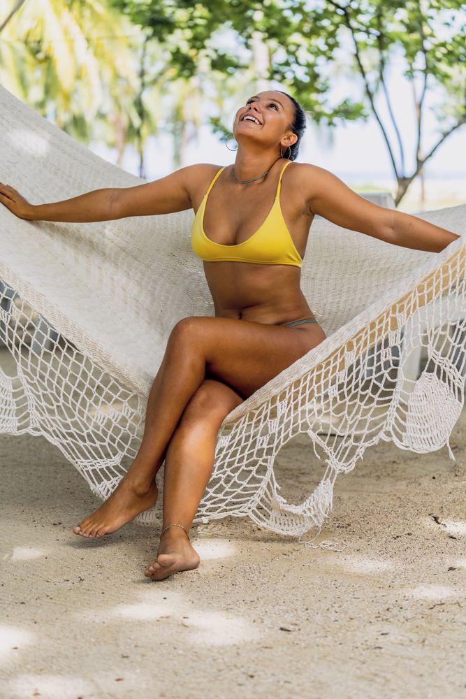 Joyful woman in bikini resting in hummock on beach