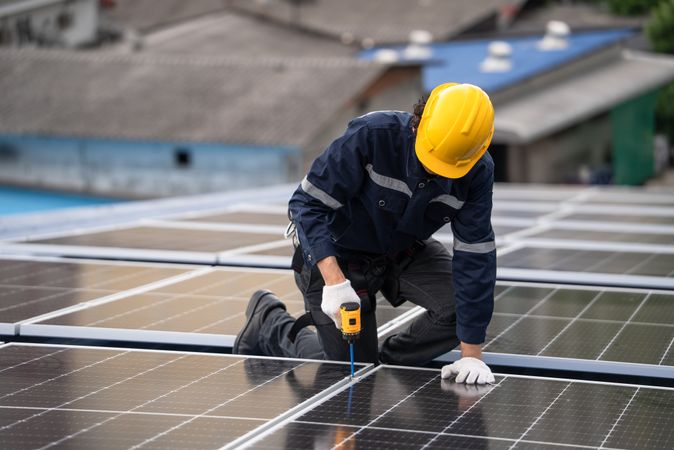 Engineer worker using electric drill repairing on solar cell panel on the roof of the factory. After service and security for industrial renewable energy concept