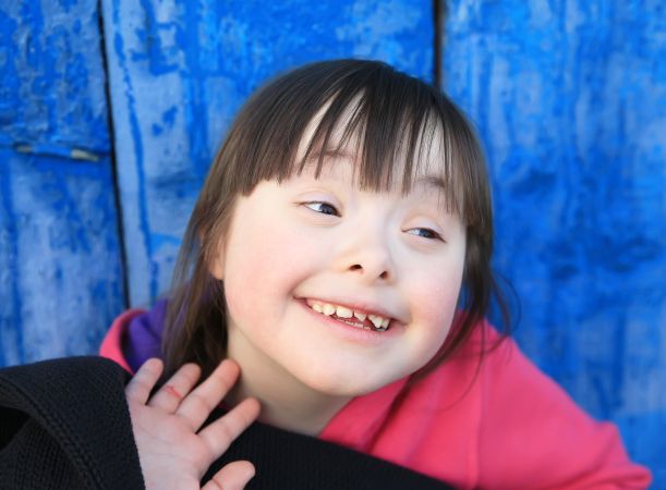 A girl with an intellectual disability smiling against a bright background