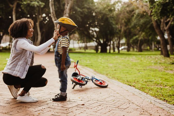 Mother helping son wearing helmet for cycling at park