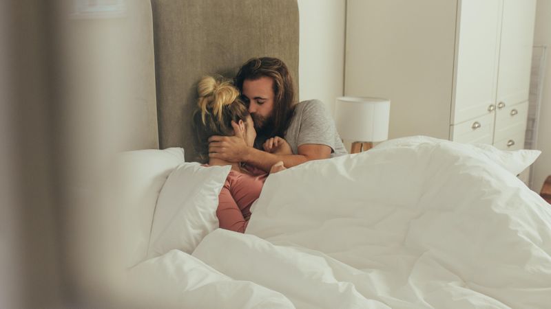 Man kissing his wife while lying in bed at home