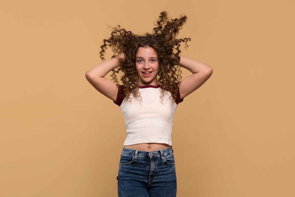 Playful young girl lifting hair with both hands, smiling energetically