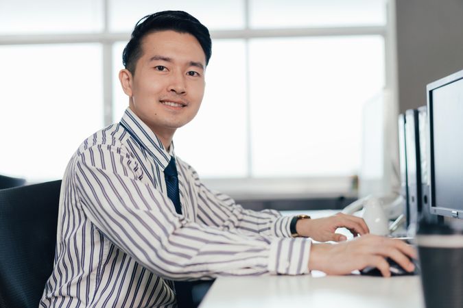 Happy Asian male employee working on computer at desk in the office